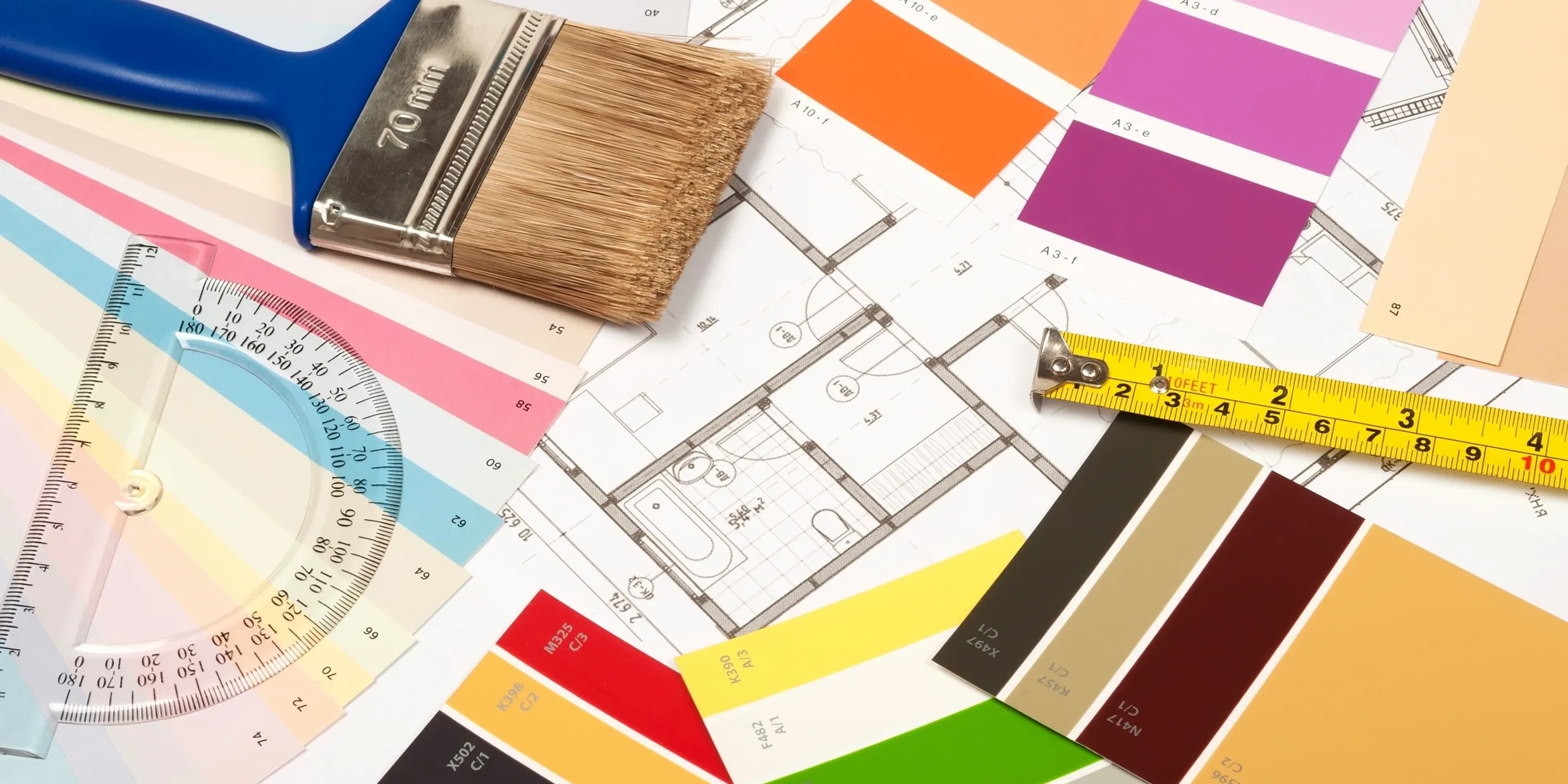 A paintbrush and measuring tape resting on floor plans and color swatches