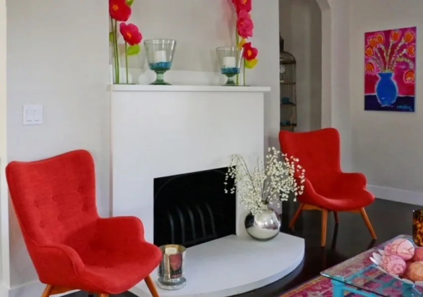 Two red accent chairs beside a white fireplace