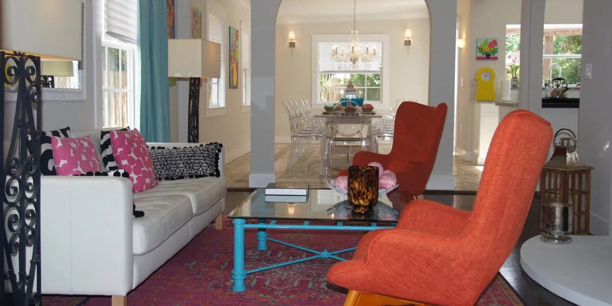A bright living room with orange chairs and pink accent pillows